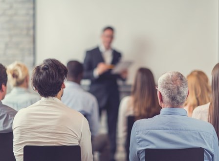 Group of people sat in a room watching a man present stood up