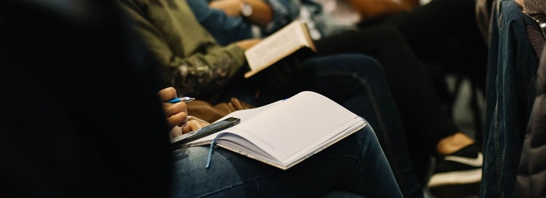 Open notebook on a lap of a person in a conference room.