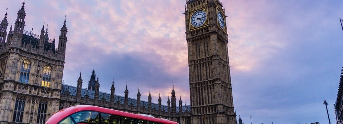 Westminster palace with a red double decker bus driving past.