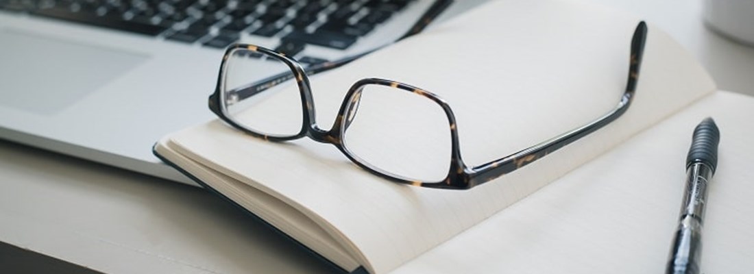 Pair of glasses resting on an open notepad and laptop.