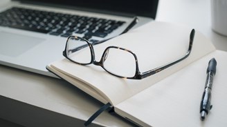 Pair of glasses resting on an open notepad and laptop.