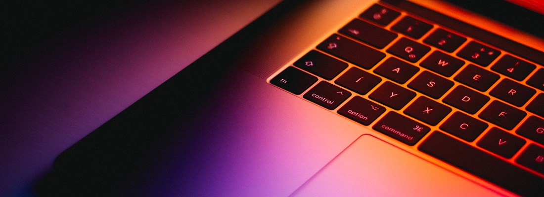 Laptop half opened with purple and orange light reflecting on the keyboard.
