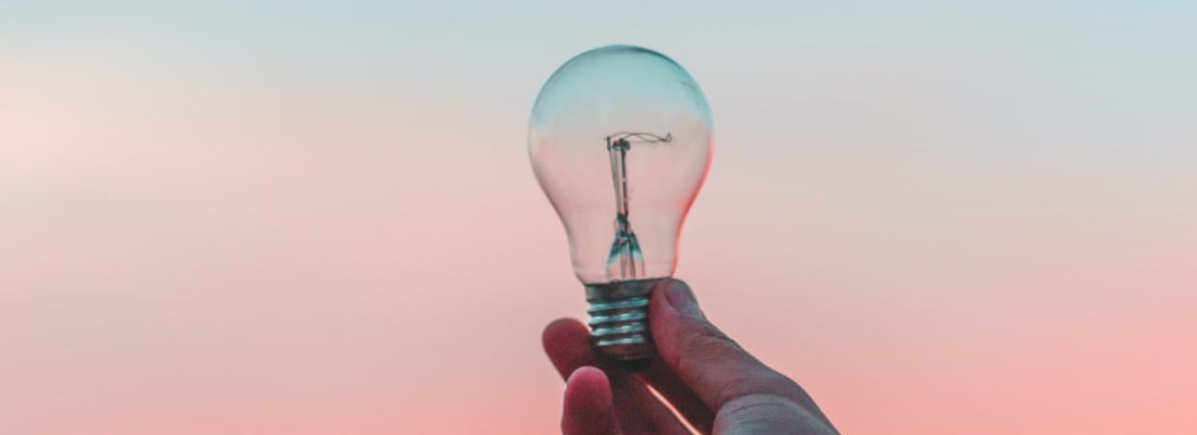 Hand holding a lightbulb up to a blue and pink sky.