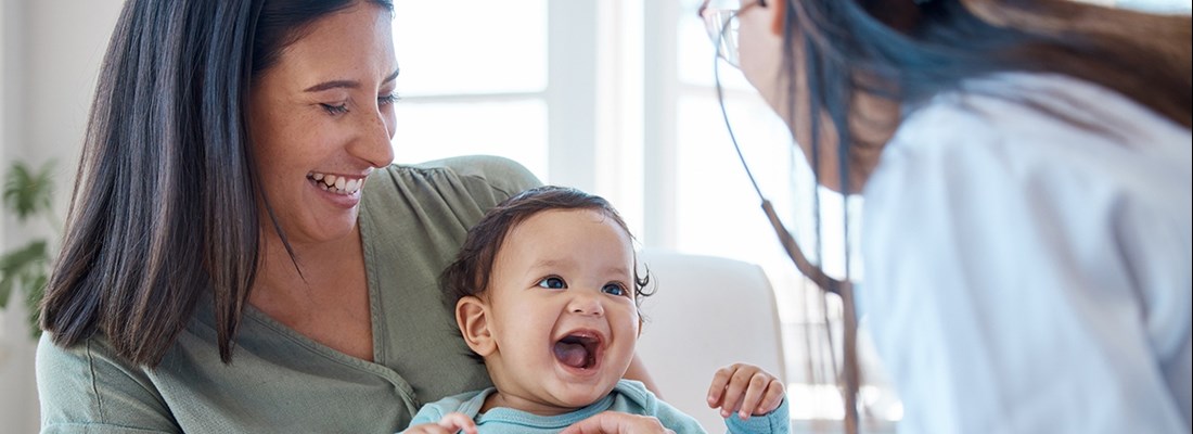 Healthcare professional using a stethoscope to examine a baby on an adult's lap during a medical check-up