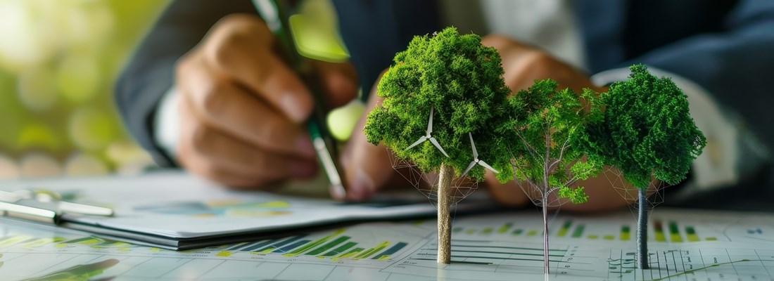 Business professional writing on a clipboard with charts, graphs, and model trees representing sustainability or financial growth